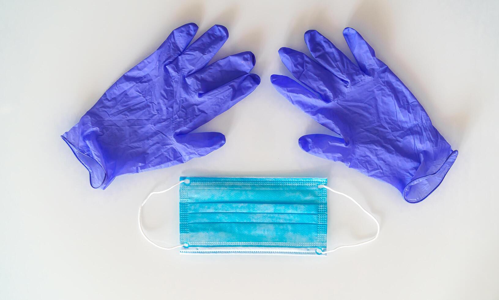 Blue disposable medical face mask and pair of nitrile powder free medical gloves on a white background photo