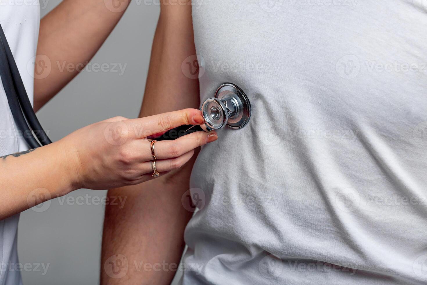 Woman's hand holding stethoscope on male's chest in white t-shirt and examining him. Female doctor is using a stethoscope to check lungs of a young man. Close-up photo