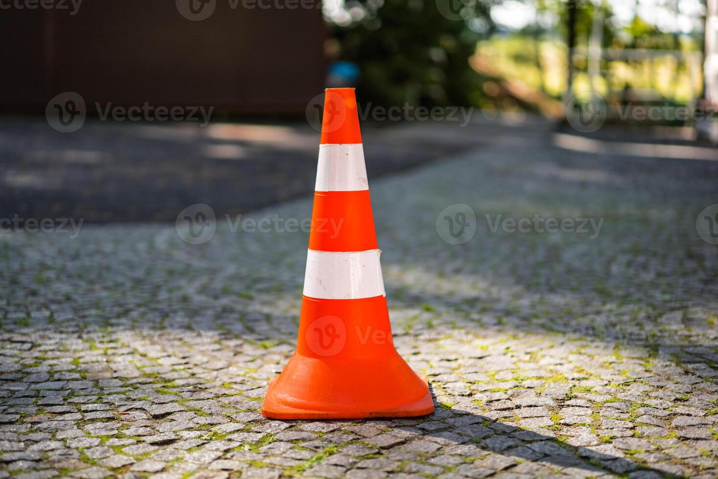 Red orange cone with a white stripe on the paving stone road. Drive safety and constructions concept. Closeup. Blurred background. photo