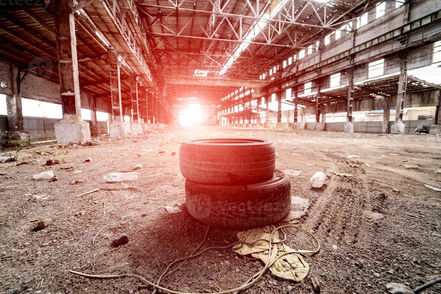 An abandoned industrial interior in grey colors. Two old tyres in a center. Broken windows and high roof. Old warehouse. photo