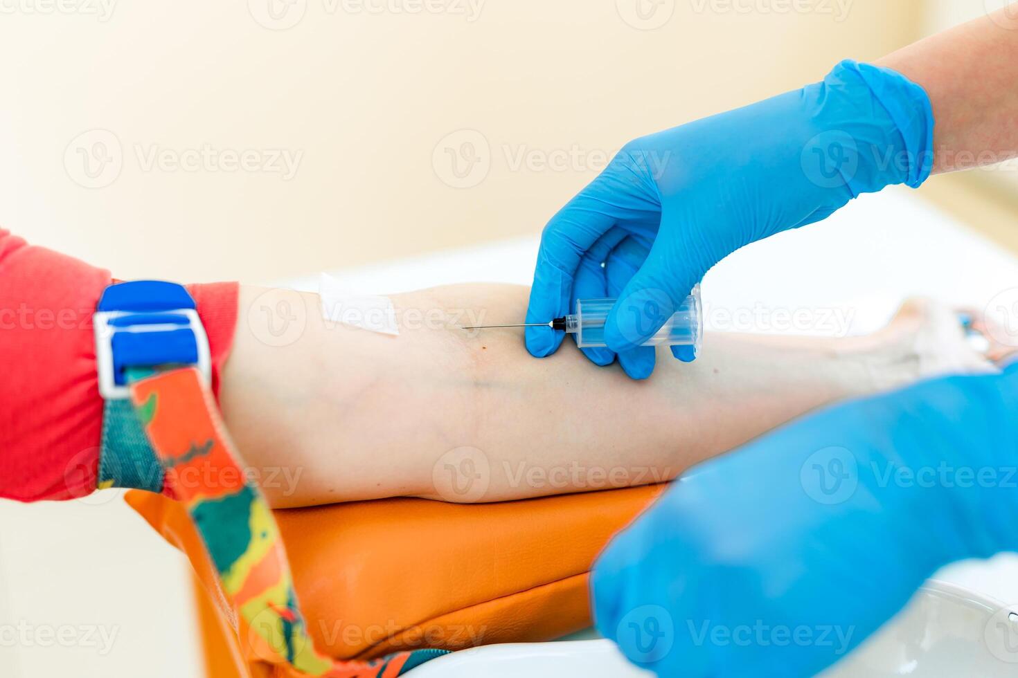 Nurse is pricking needle for the syringe into the patient's arm to take blood sample in a lab. Woman's hands in protective blue gloves makes an injection into a vein. Close-up. photo