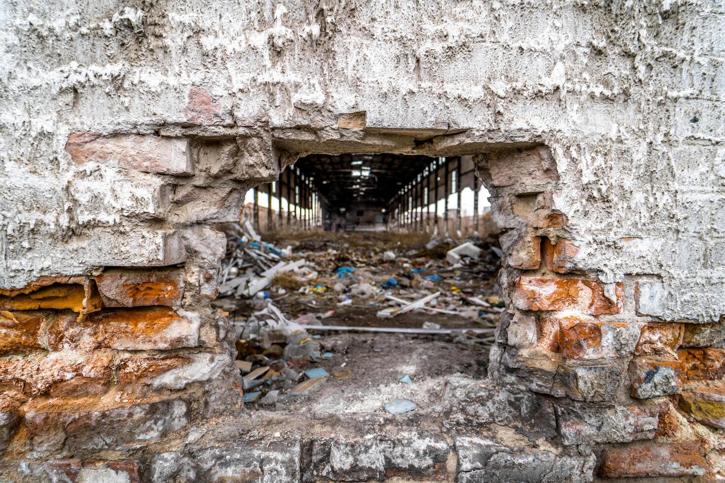 Hole in a wall into the old destroyed factory with a lot of broken debris inside. Ruined brick wall of the building outdoors after the military actions. photo