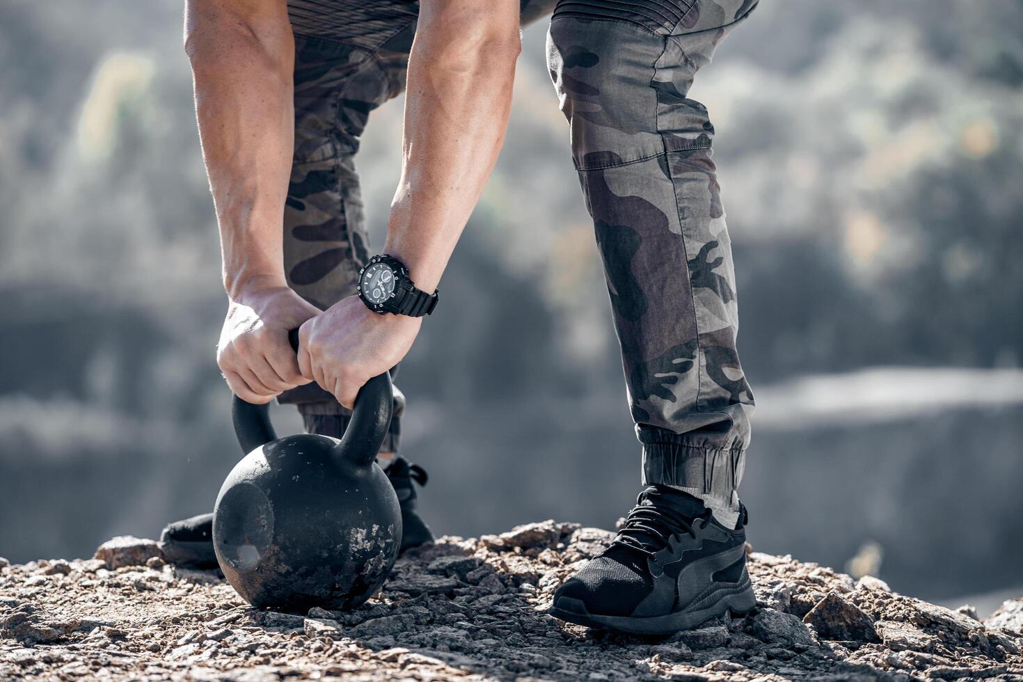 fuerte masculino brazos en el pesas rusas de 24 kilos. muscular manos con un reloj en el peso. fisicoculturistas manos y piernas cerca arriba en el roca. foto