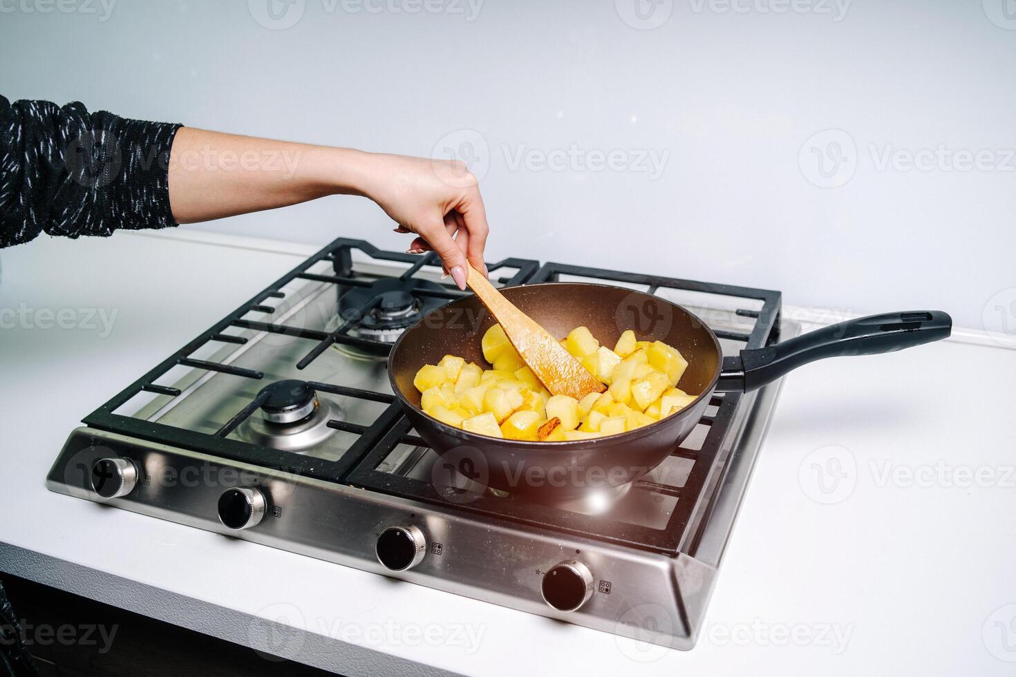 un mujer fritura patatas en el cocina. frito patata porciones foto