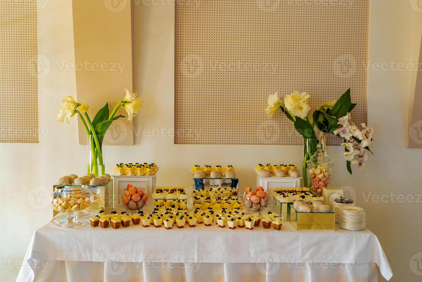 candy bar. A festive table with panakota, macaroons, muffins,meringues and with two vases with beautiful flowers is located near the wall at the wedding in the restaurant photo