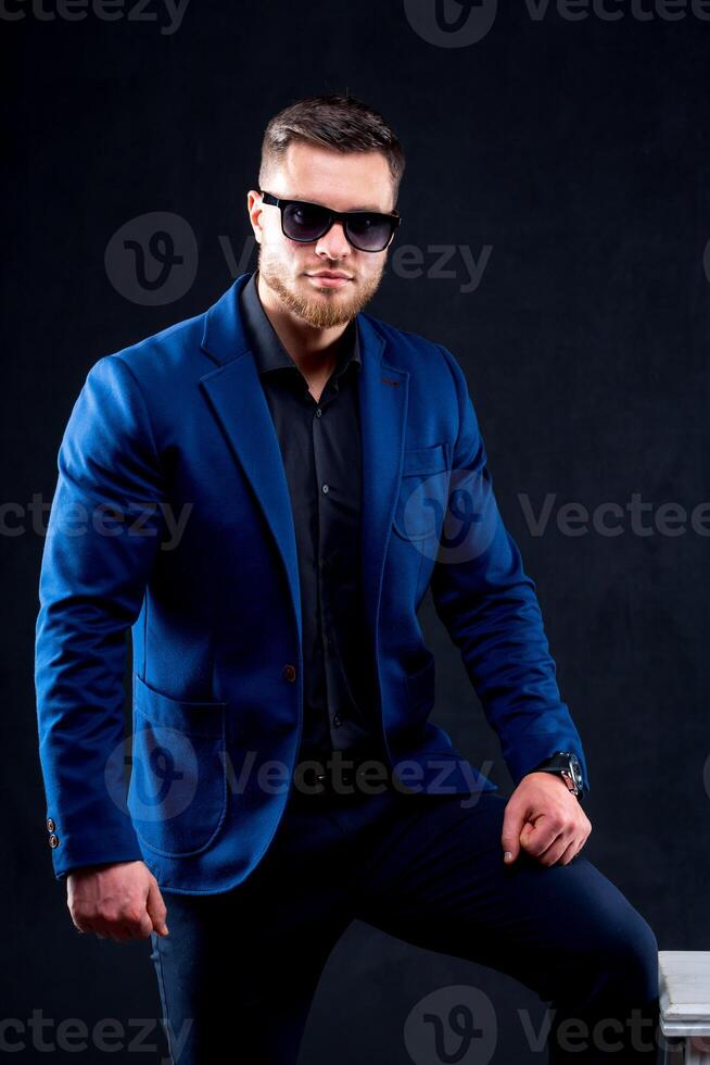 A confident elegant handsome young man standing in front of a black background in a studio wearing a nice suit photo