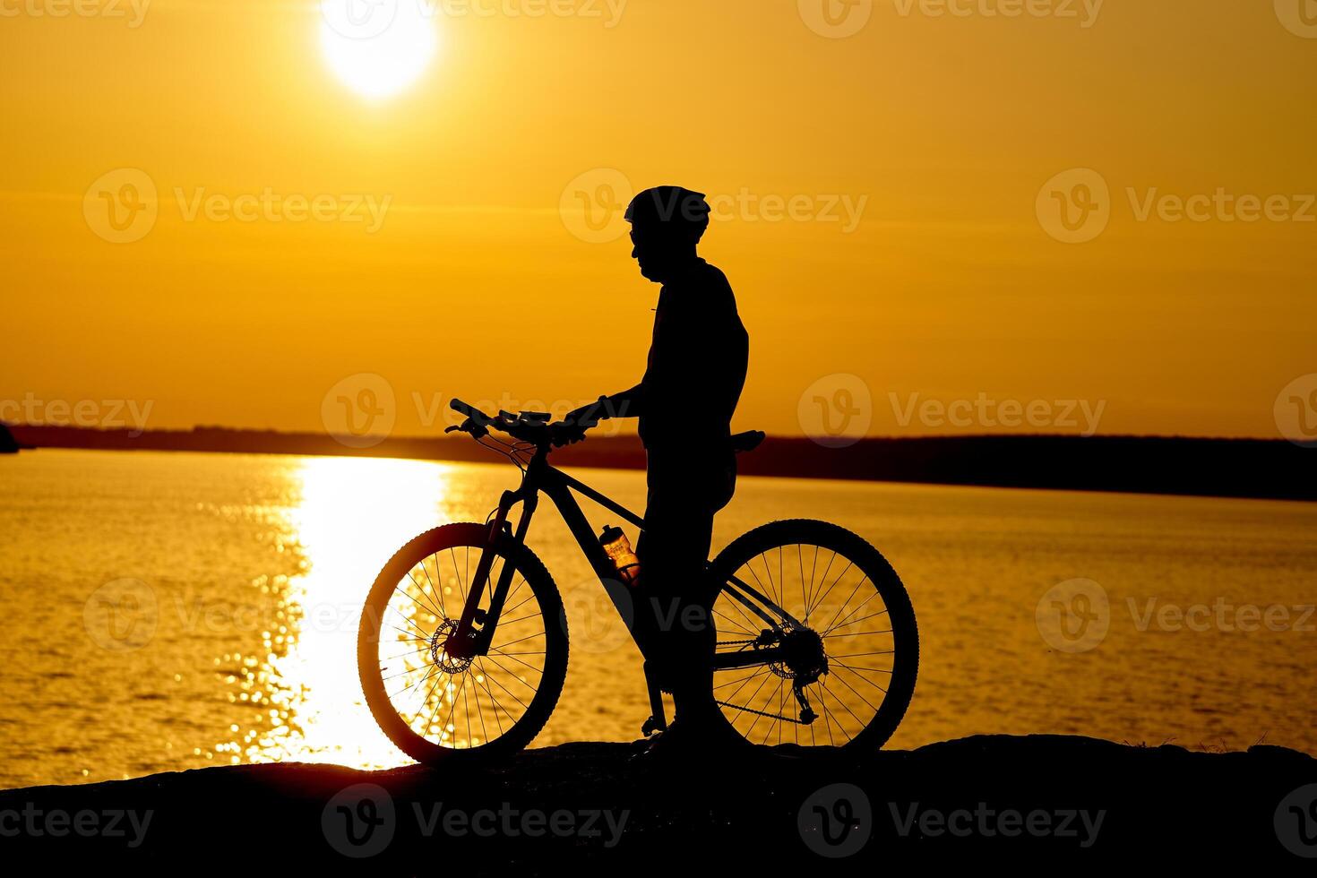 Silhouette of a male cyclist with helmet at sunset near the river. Healthy active lifestyle photo