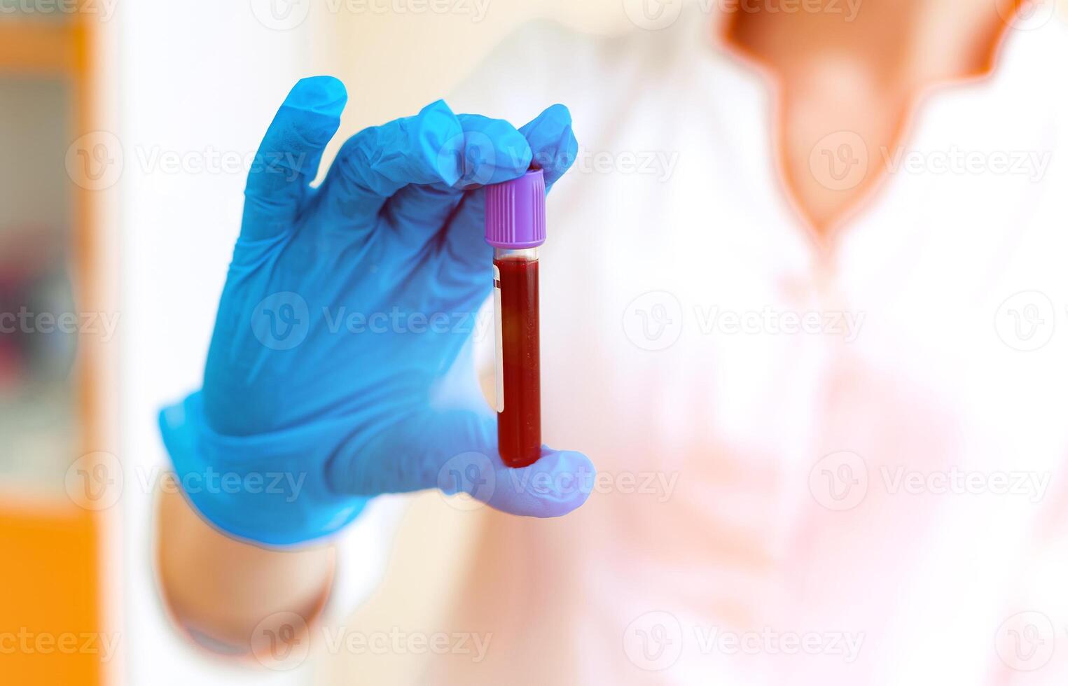 Vial full of blood in the hand of a laboratory specialist. Woman's hand in blue protective glove is holding a test tube with red liquid. Close-up. photo