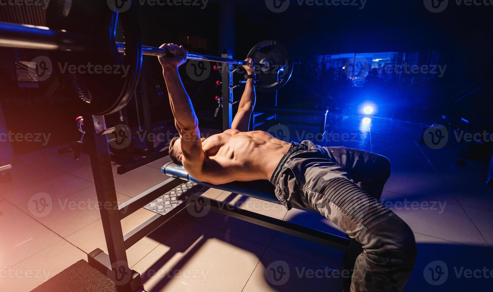 Fit young man lifting barbells doing workout at a gym. Sport, fitness, weightlifting, bodybuilding, training, athlete, workout exercises concept. View from the side. photo