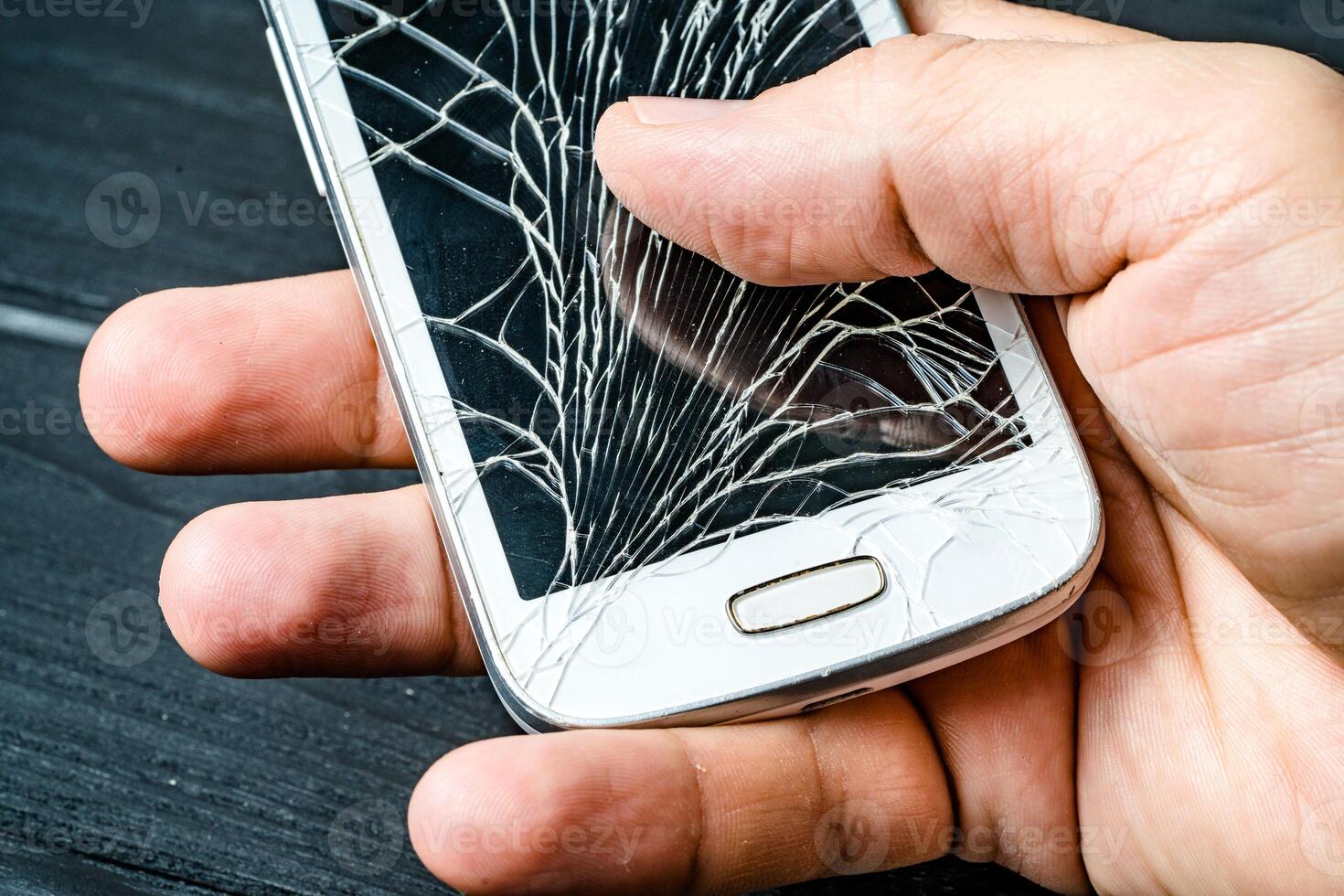 Man's hand holding mobile phone with broken screen over the dark background. Smart phone with glass broken touch screen in man's hand. Close-up photo