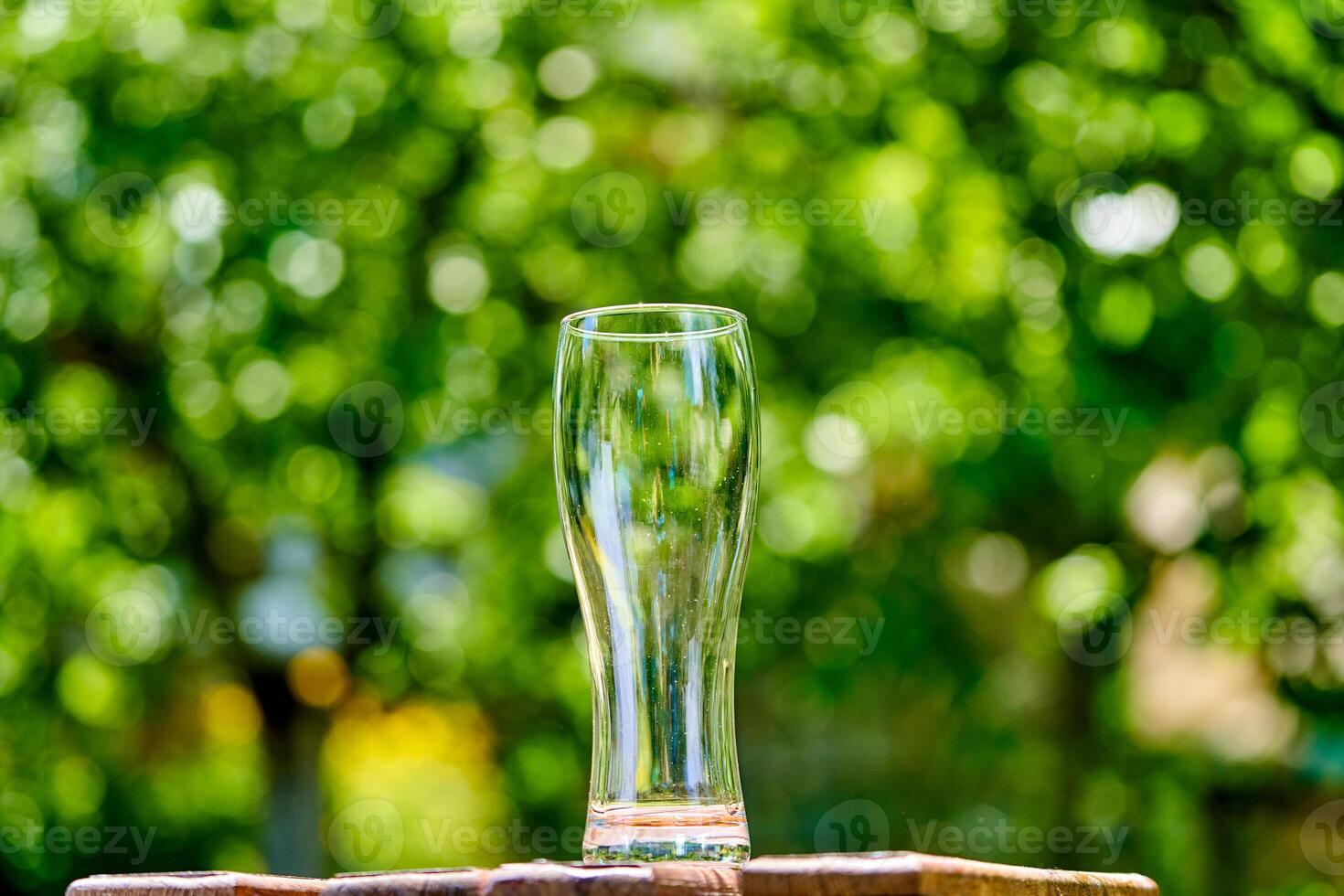 Empty glass of beer on wooden table on green nature background photo