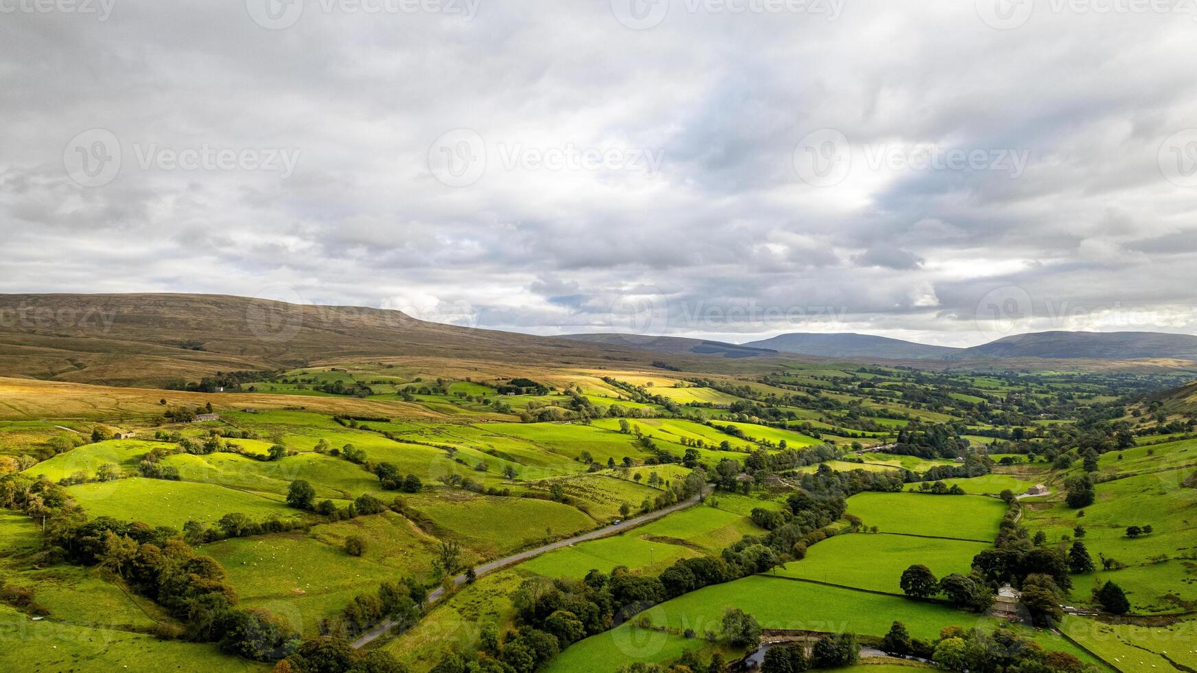 Aerial view of a lush green countryside with patchwork fields under a cloudy sky. photo