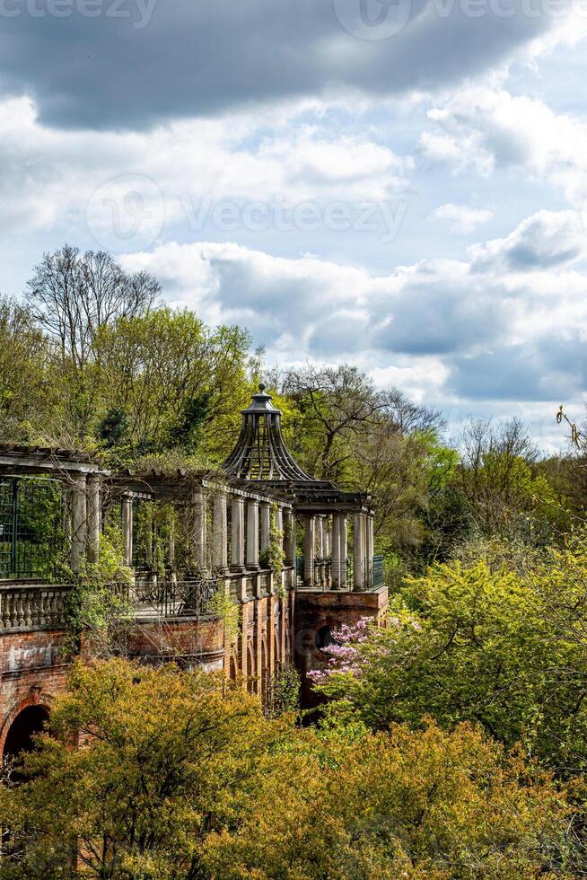 Ruined classical architecture with columns amidst lush greenery under a cloudy sky. photo