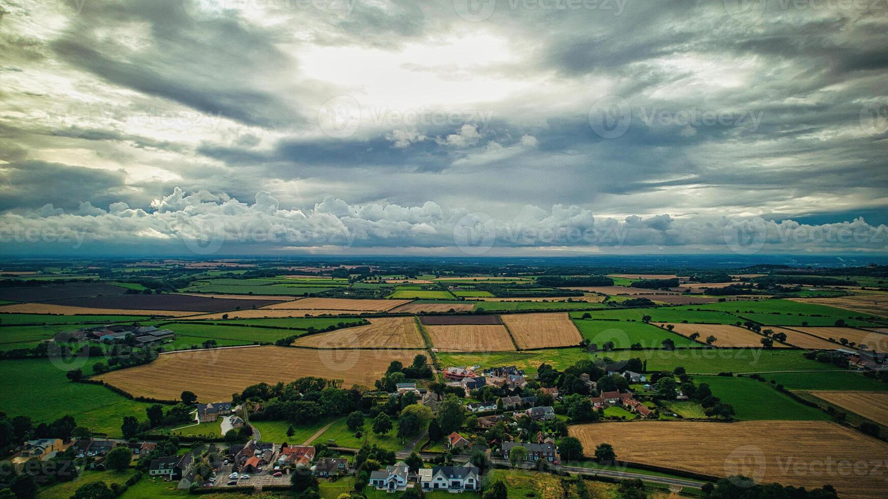 Dramatic clouds over a serene rural landscape with fields and a small village in Yorkshire Moors. photo