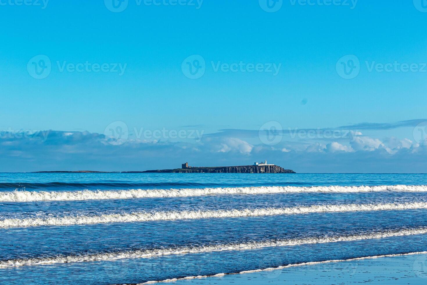 Tranquil seascape with gentle waves and distant island under a clear blue sky. photo