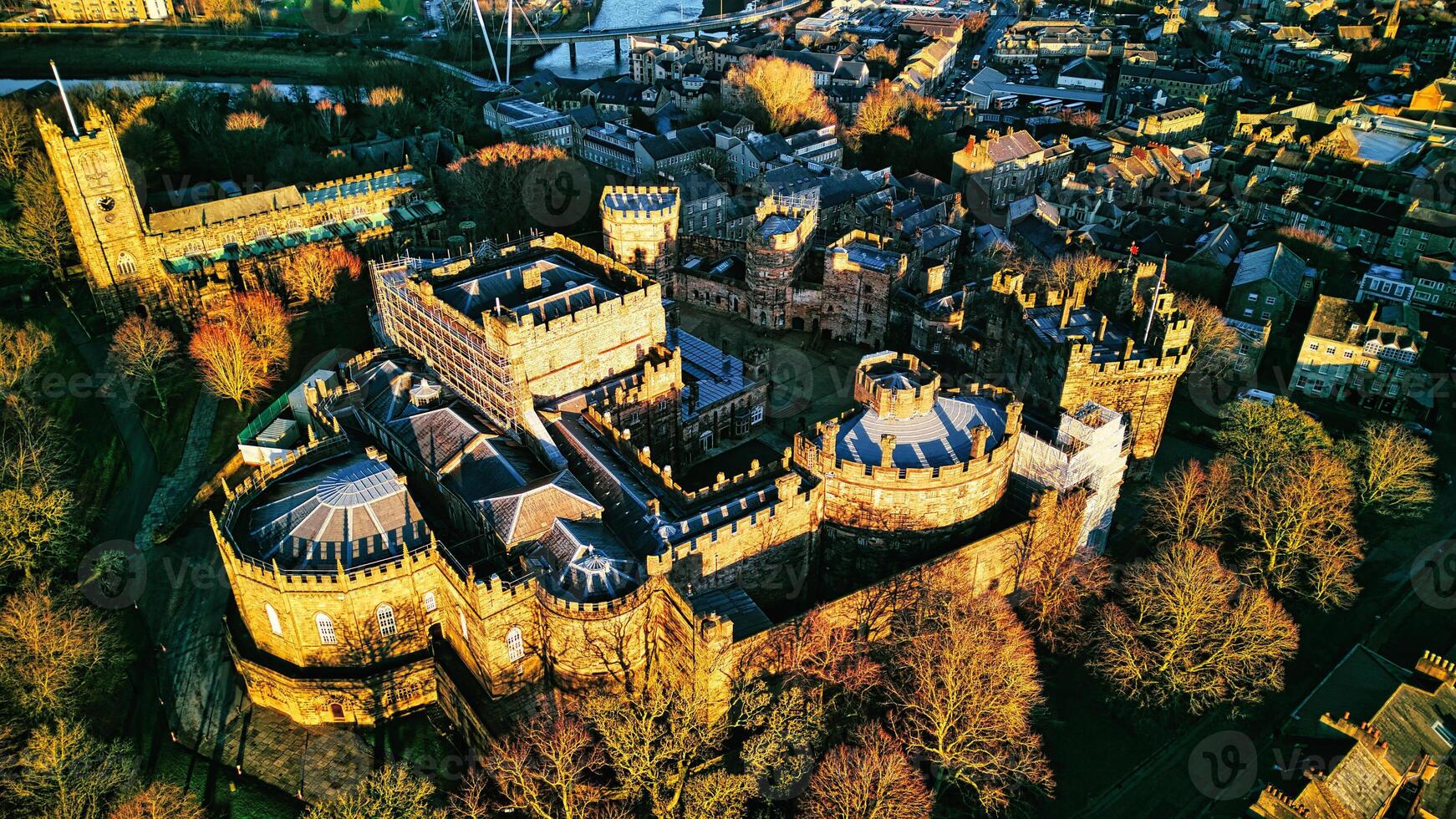 Aerial view of a majestic medieval Lancaster castle at sunset, with surrounding greenery and town in the background. photo