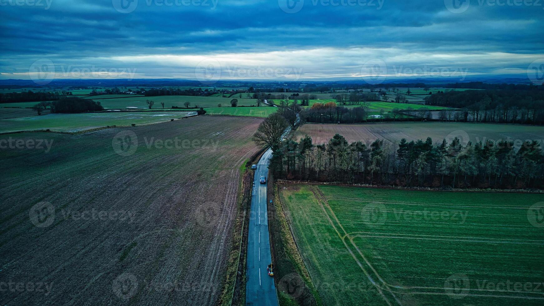 Aerial view of a serene rural landscape with a narrow river cutting through fields and forests under a cloudy sky. photo