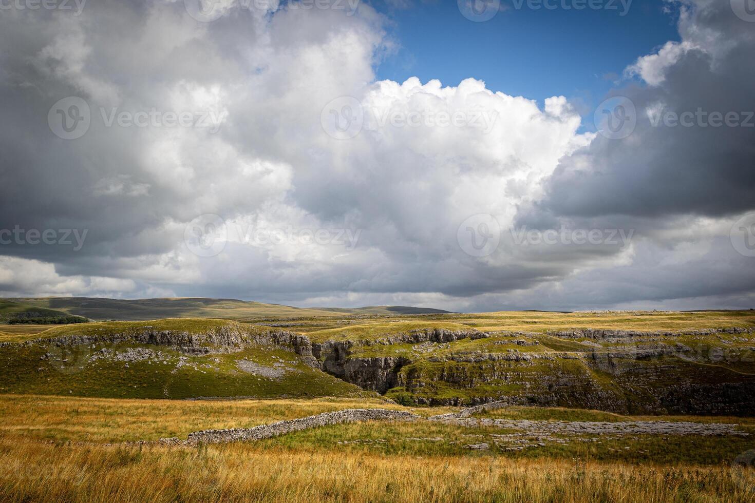 Dramatic landscape with expansive grasslands and rugged cliffs under a cloudy sky. photo