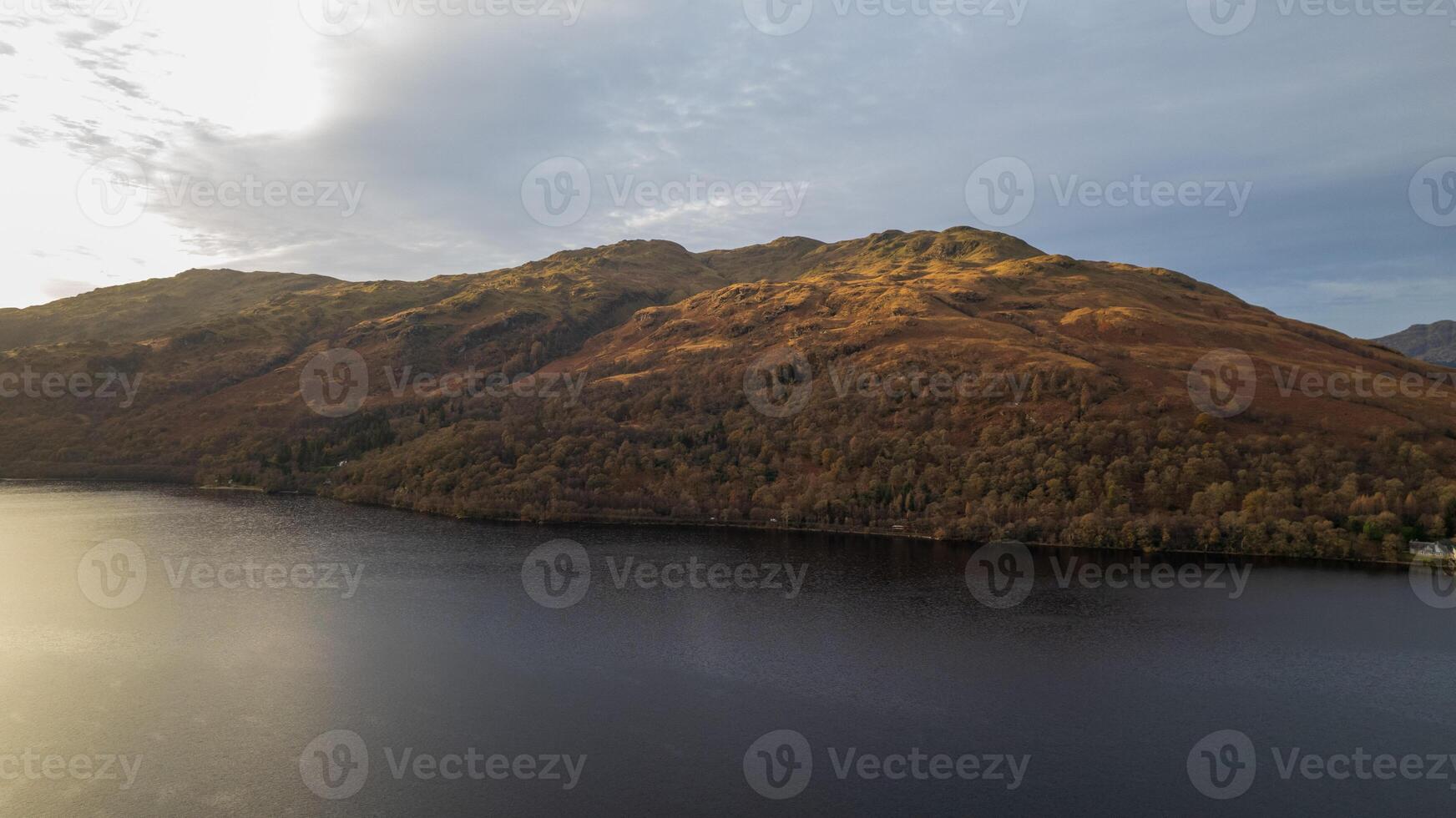 Serene lake with sunlit autumnal hillside, reflecting warm colors in the calm water at dusk. photo