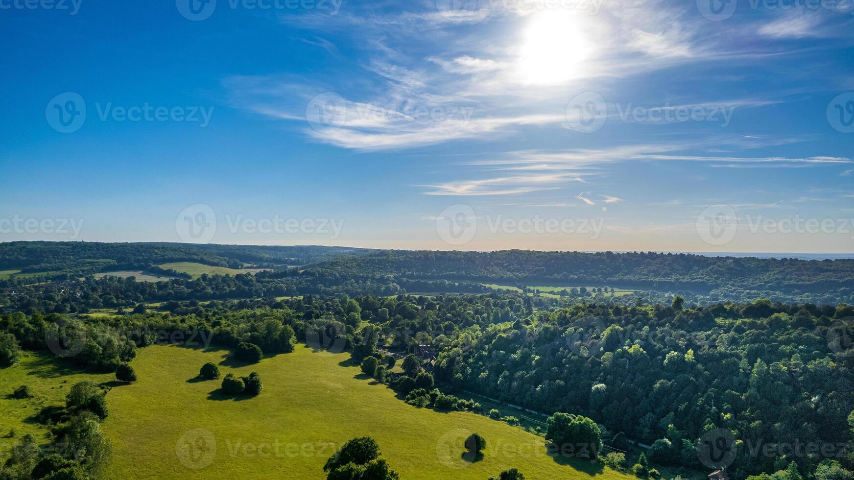 Aerial view of lush green countryside under a clear blue sky with scattered clouds. photo