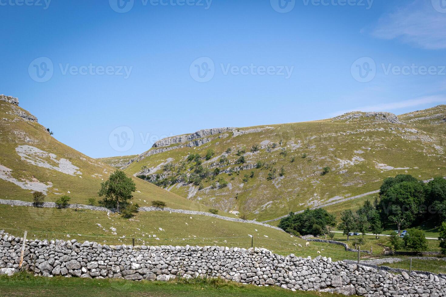 Idyllic rural landscape with stone walls and rolling hills under a clear blue sky. photo