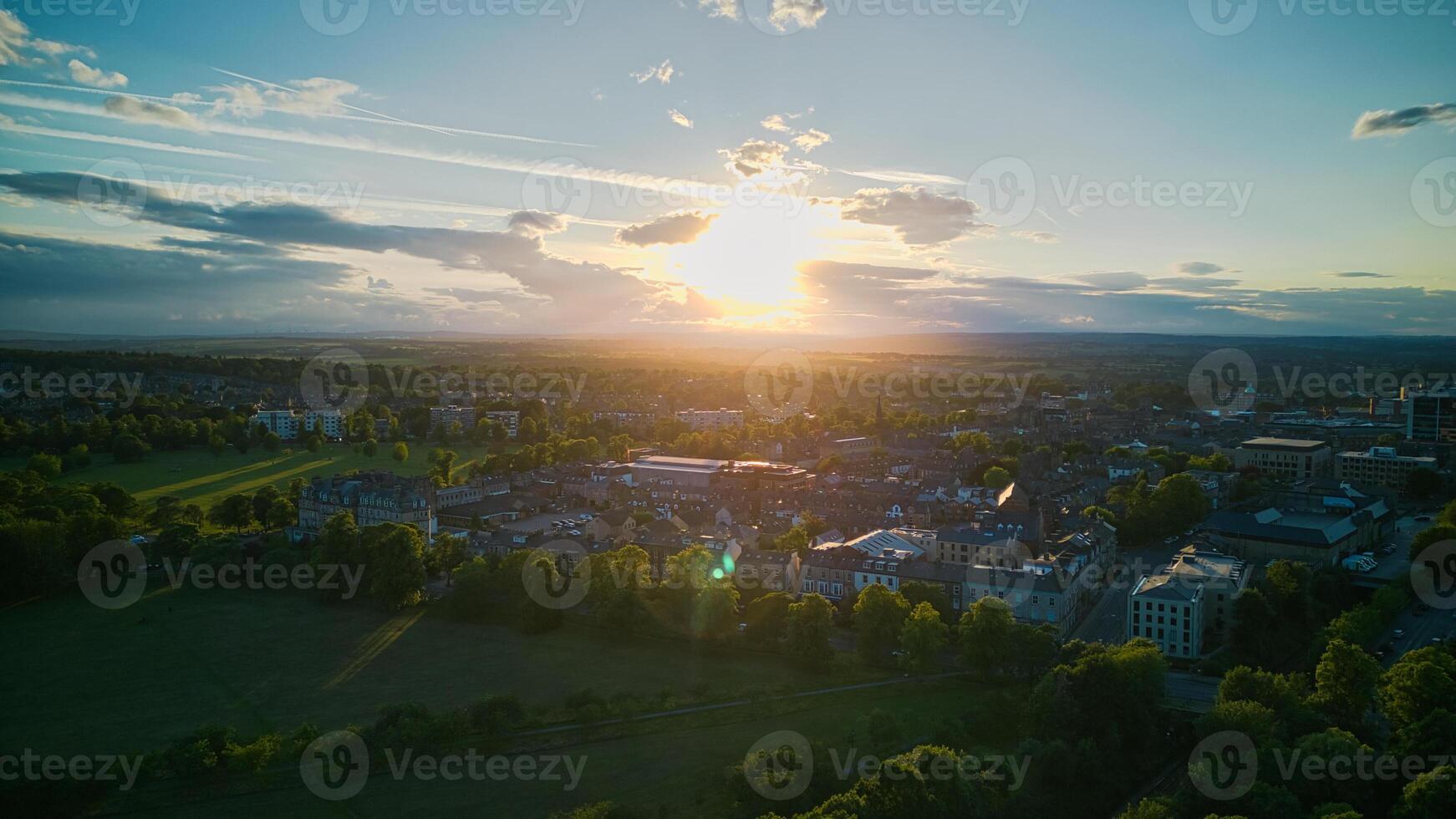 Aerial view of a cityscape at sunset with sun rays piercing through clouds, highlighting green spaces and urban buildings in Harrogate, North Yorkshire. photo