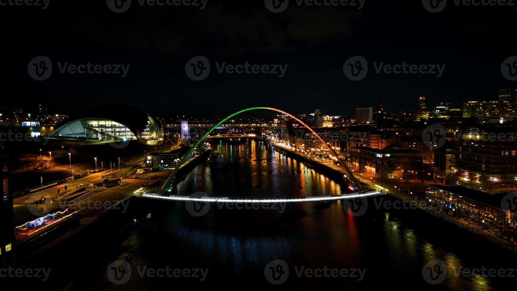Night cityscape with illuminated arch bridge over river, reflecting lights on water with urban skyline in Newcastle upon Tyne photo