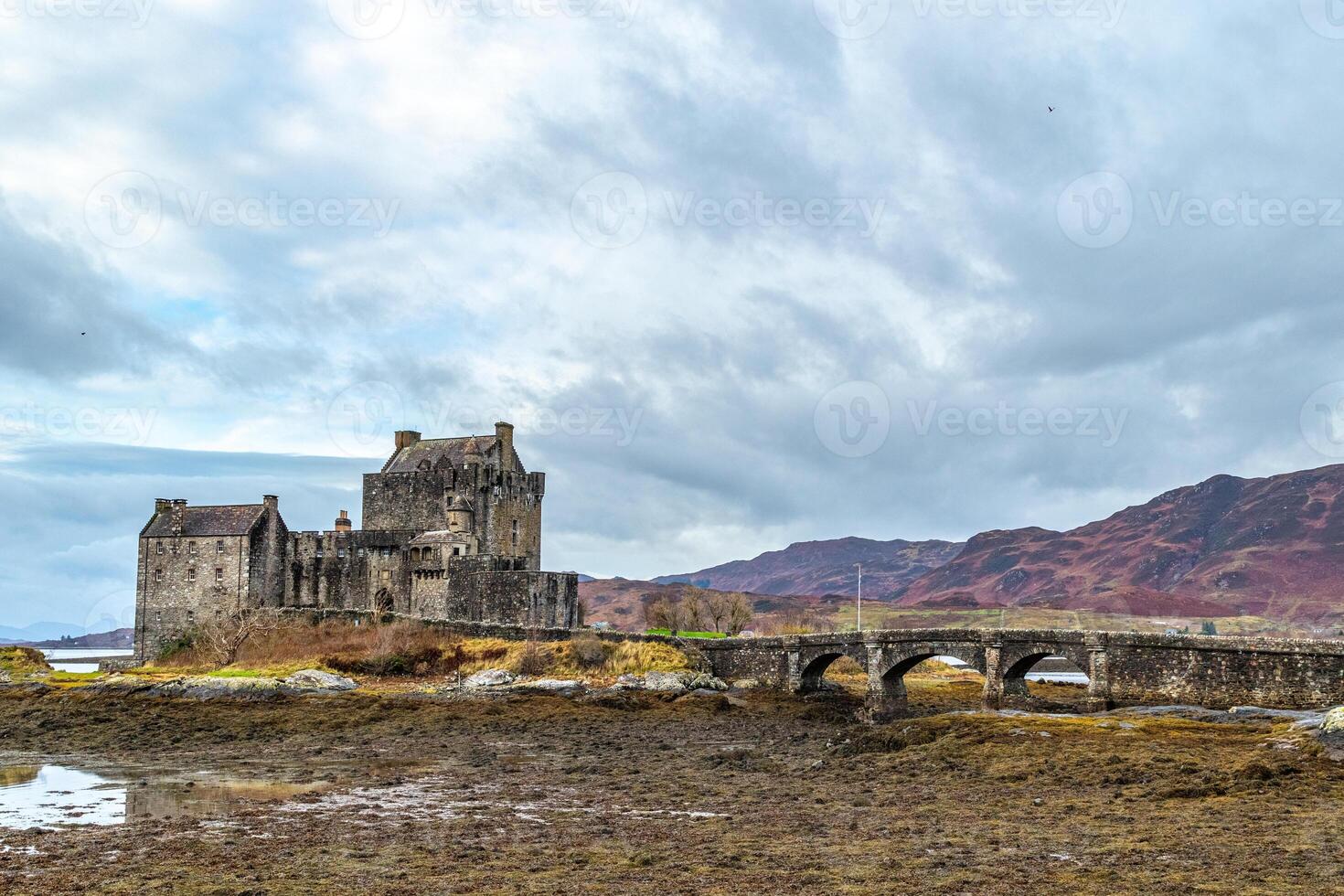 Medieval castle with stone bridge against a dramatic sky, surrounded by rugged landscape and autumn colors in Scotland. photo