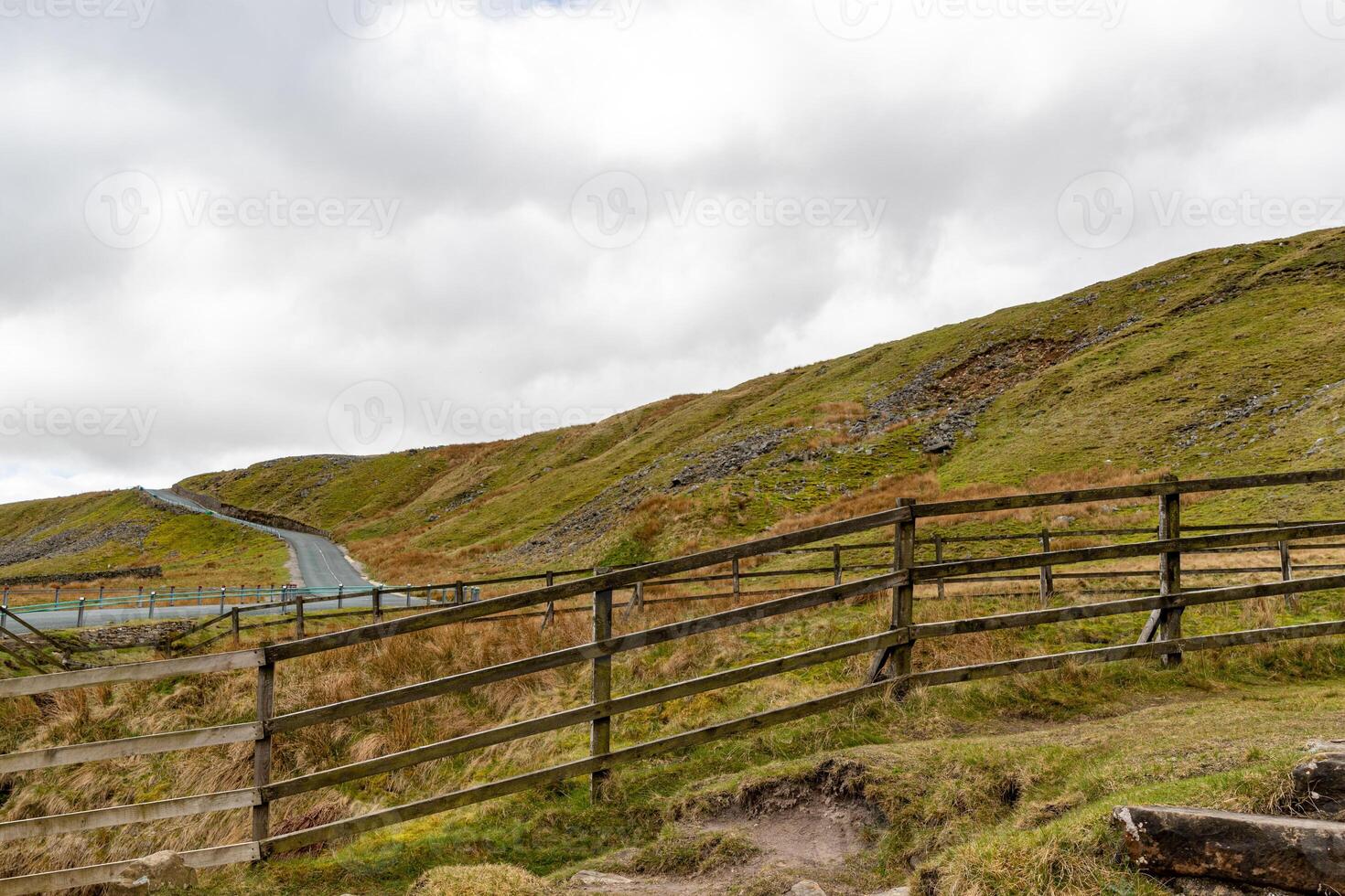 Rustic wooden fence leading into rolling green hills under a cloudy sky, depicting tranquil rural landscape in Yorkshire Dales. photo