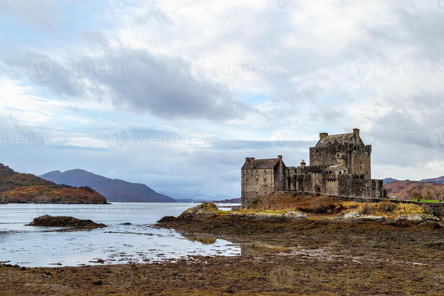 Majestic ancient castle by a serene lake with cloudy skies and mountainous backdrop in Scotland. photo