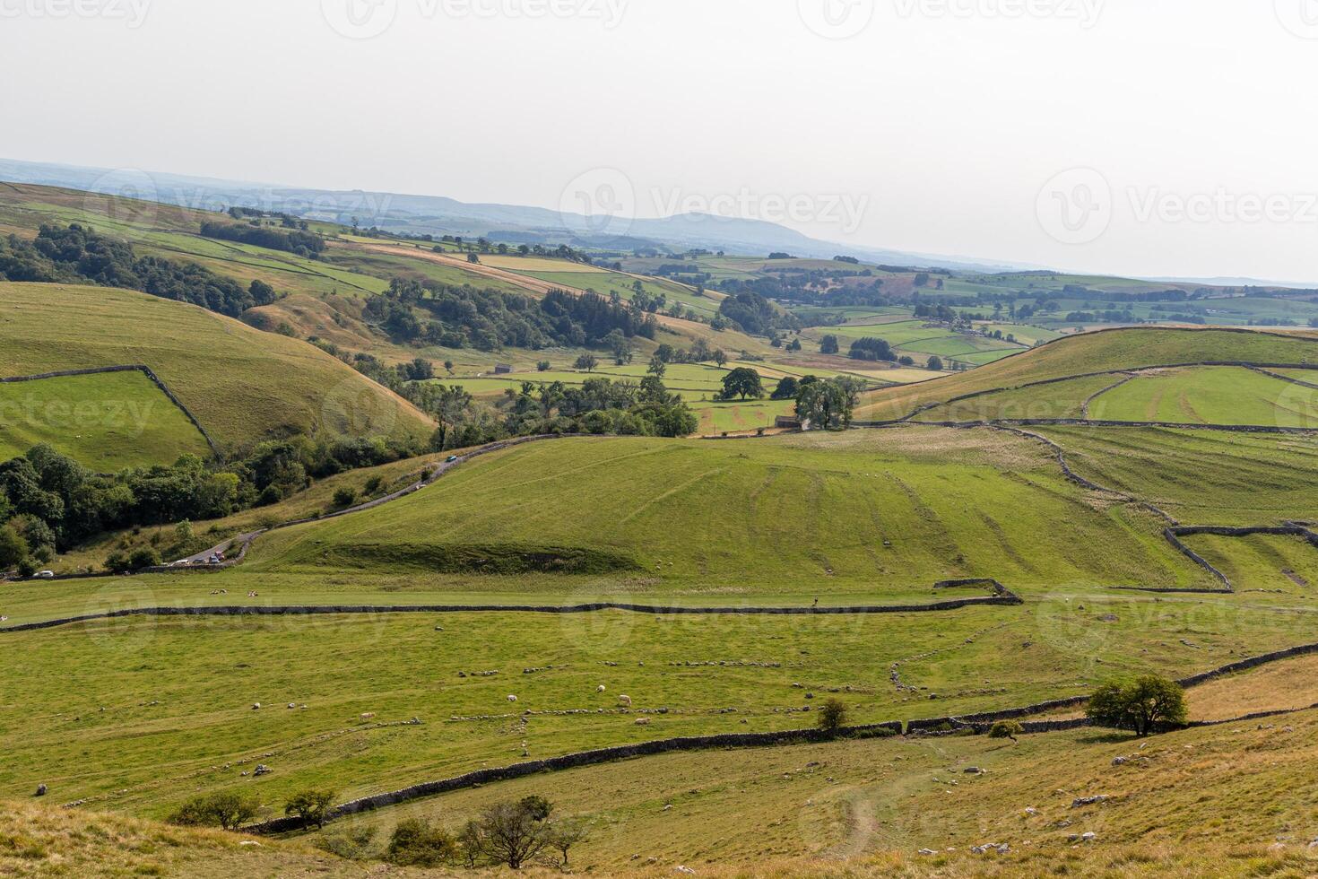 Rolling green hills with patchwork fields under a hazy sky, depicting rural farmland scenery. photo