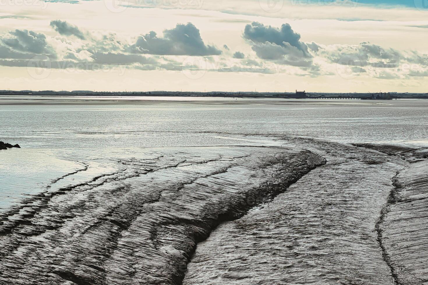 Serene coastal landscape with textured tidal patterns and a cloudy sky. photo