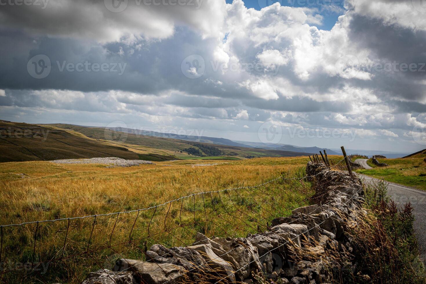 Rustic stone wall along a country road with rolling hills and dramatic cloudscape in the background. photo