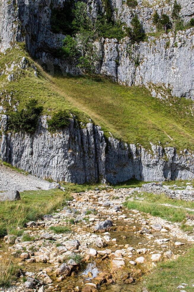 Scenic view of a rocky mountain slope with a green grassy area and a small stream in the foreground. photo