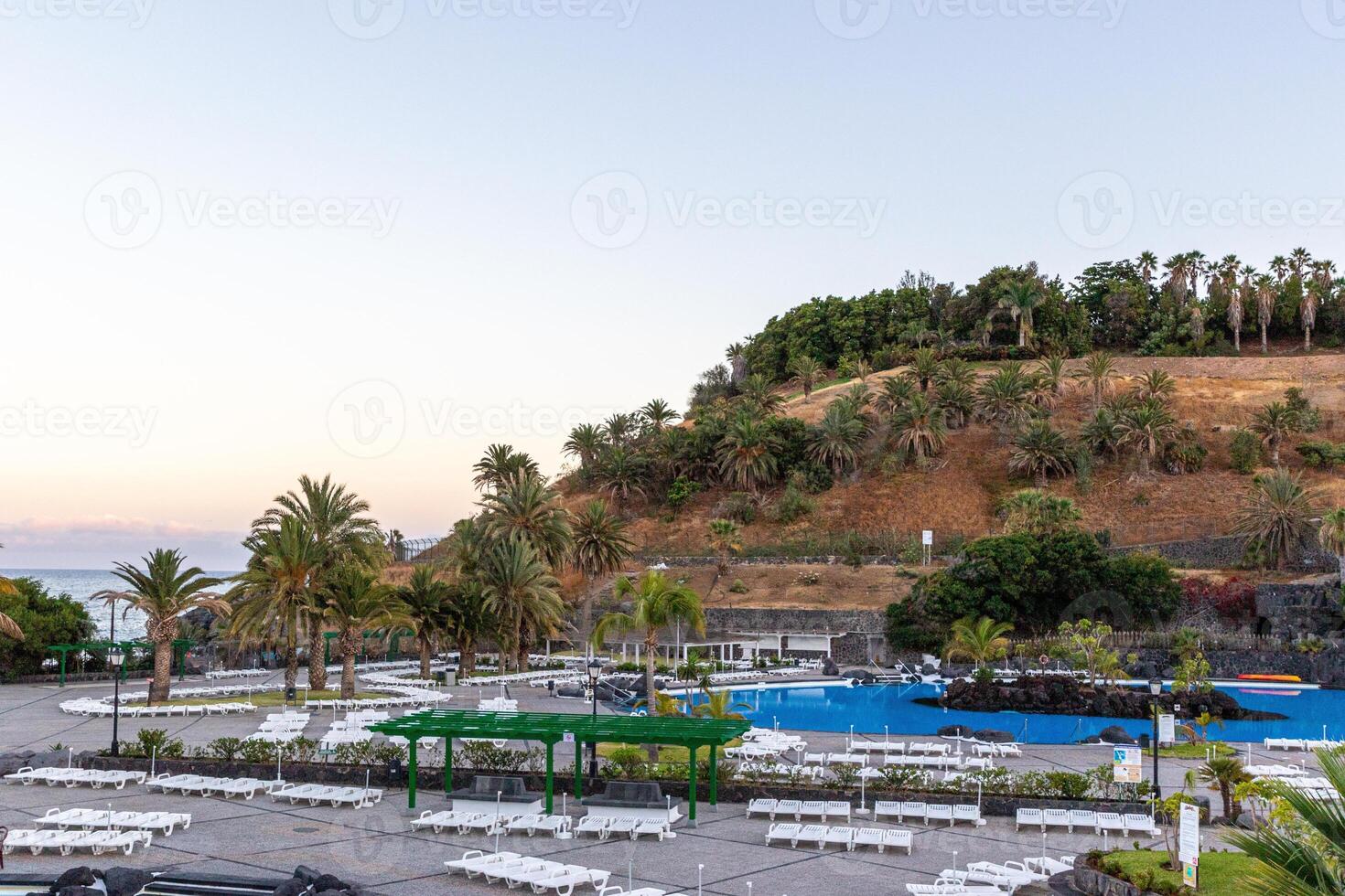 Serene resort with swimming pools surrounded by palm trees at the foot of a lush hill during twilight in Santa Cruz de Tenerife photo