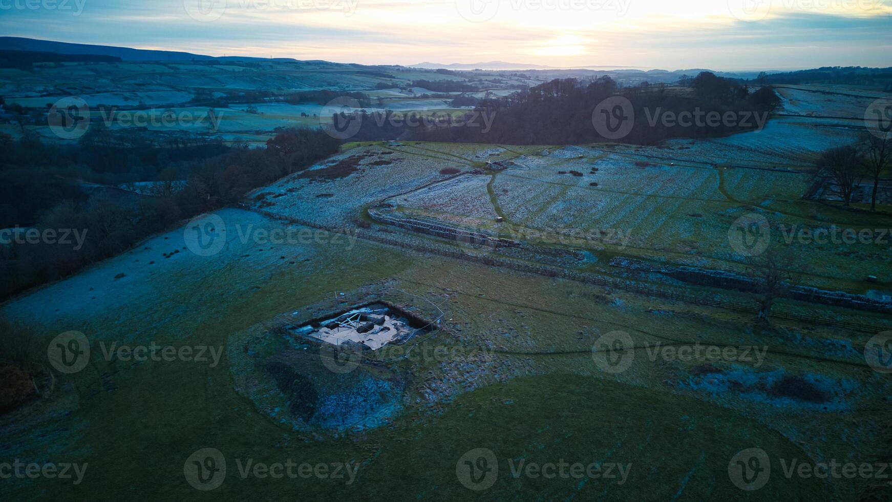 Aerial view of a tranquil countryside landscape at dusk with fields, a pond, and the horizon under a gradient sky. photo