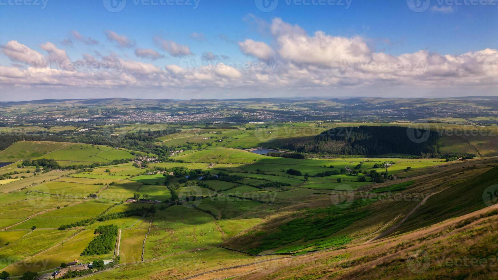 Panoramic view of a lush green valley with rolling hills under a blue sky with scattered clouds in Pendle Hill, England. photo