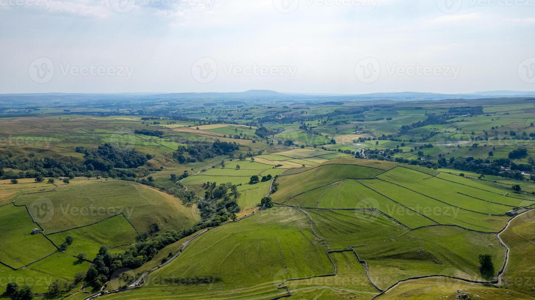 Aerial view of lush green countryside with patchwork fields and meandering roads under a hazy sky. photo