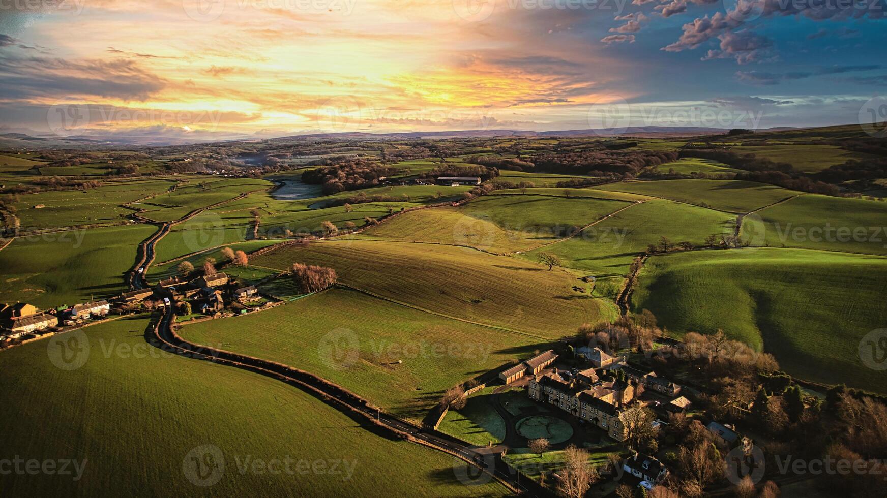 Aerial view of a picturesque rural landscape at sunset with rolling hills, a winding road, and a small village. photo