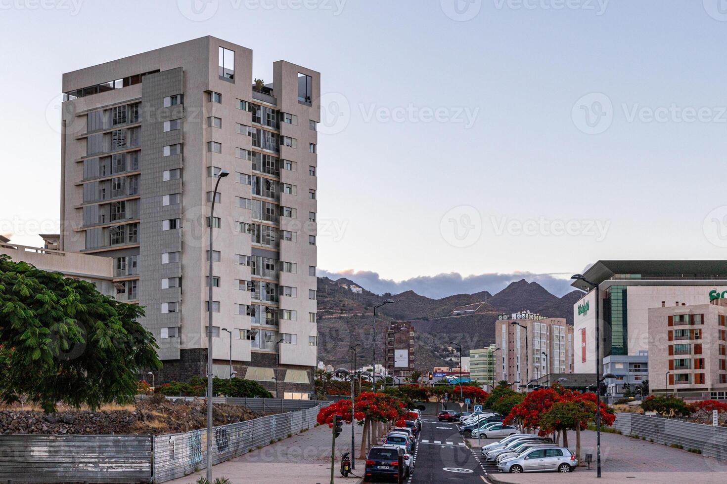 Urban street view with modern buildings, parked cars, and distant mountains at dusk in Santa Cruz de Tenerife photo