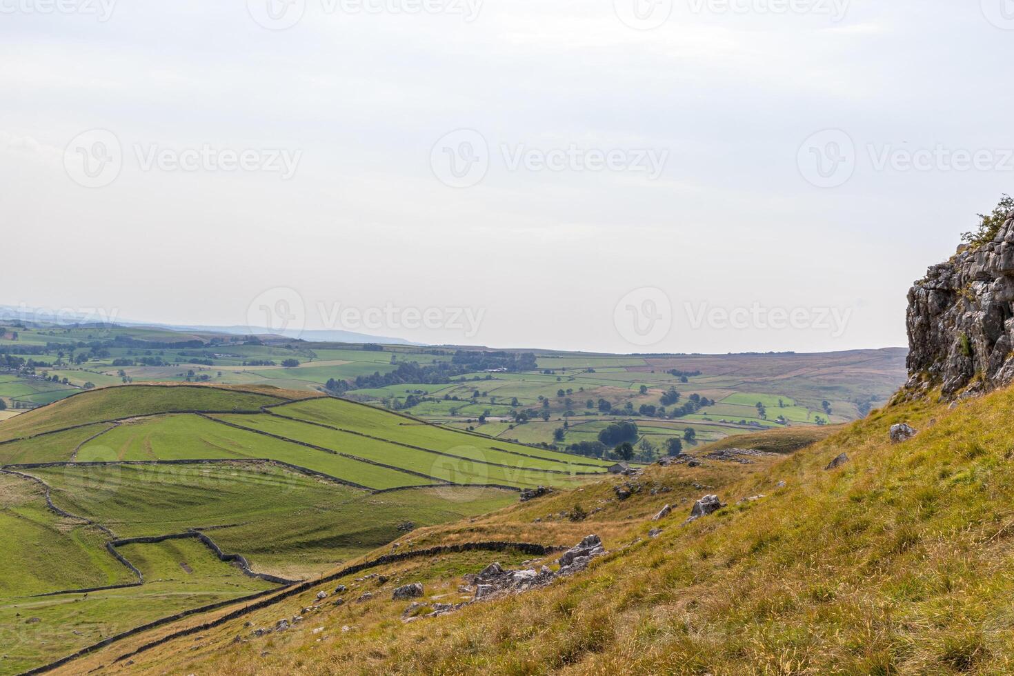 Rolling green hills with dry stone walls under a hazy sky, showcasing rural countryside charm. photo