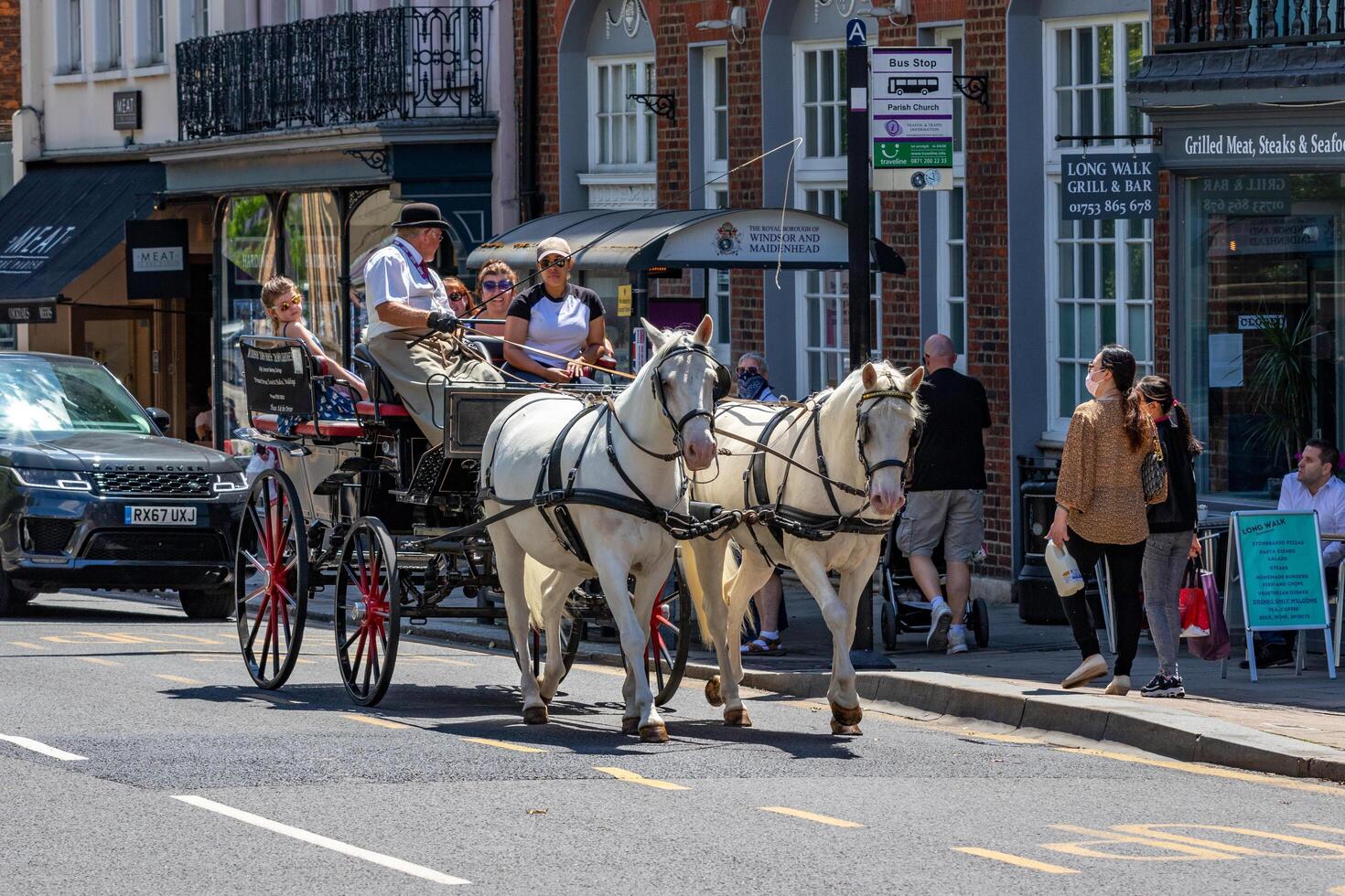 Horse-drawn carriage with passengers on a sunny urban street, flanked by modern cars and city shops. photo