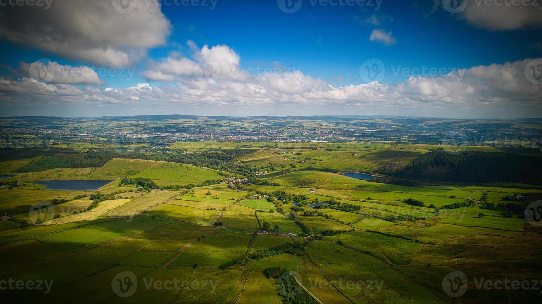 Aerial view of lush green countryside with fields, trees, and a lake under a partly cloudy sky in Pendle Hill, England. photo