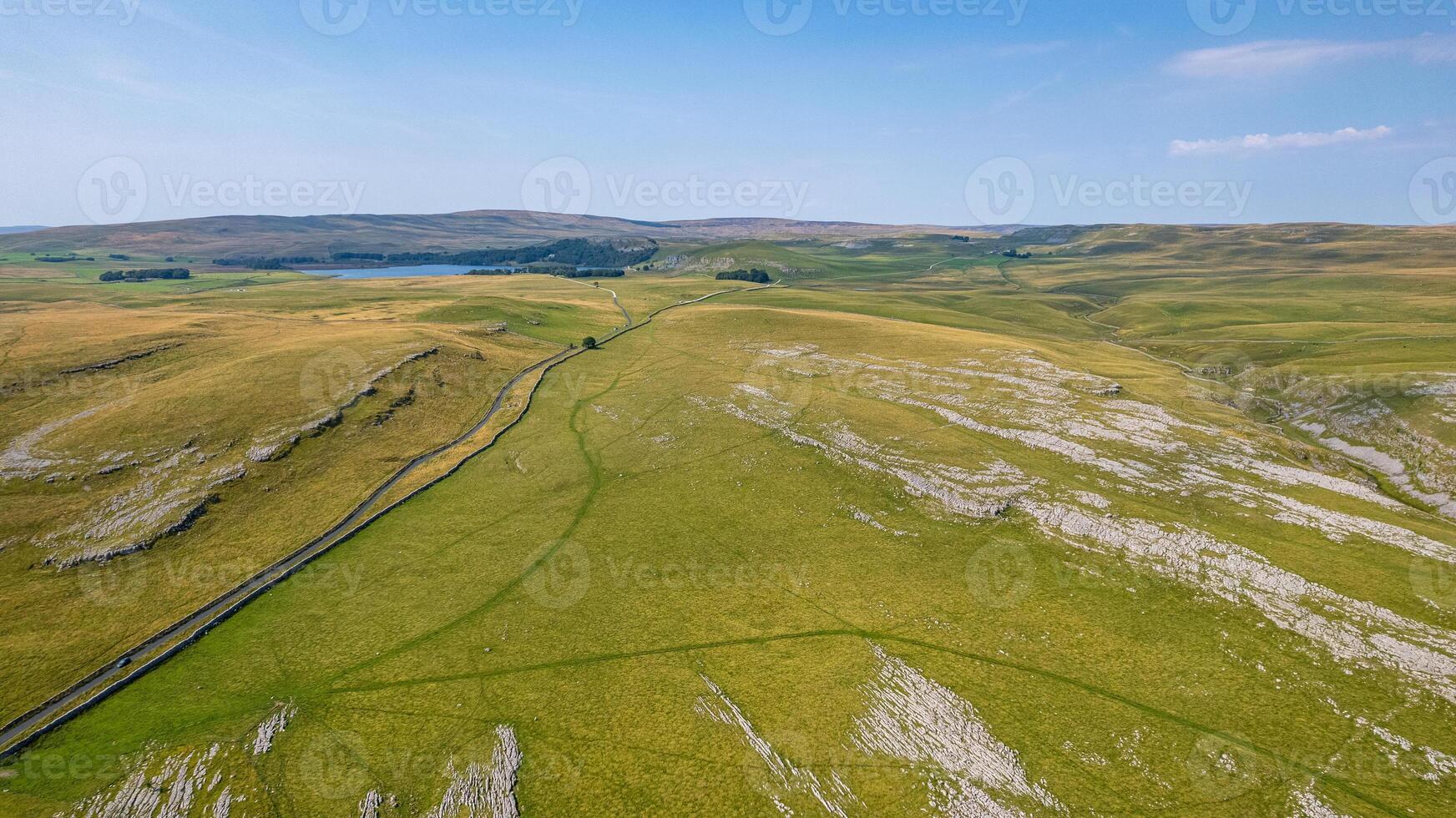 Aerial view of a lush green landscape with rolling hills and a winding road under a clear blue sky. photo