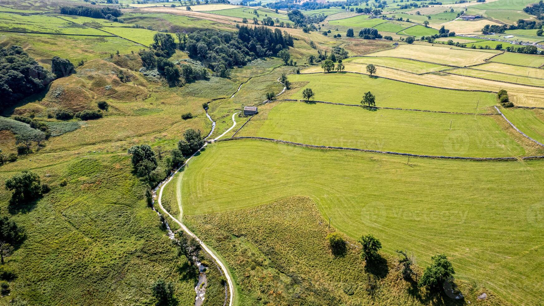 Aerial view of a winding country road through green fields and pastures with patchwork landscape patterns. photo