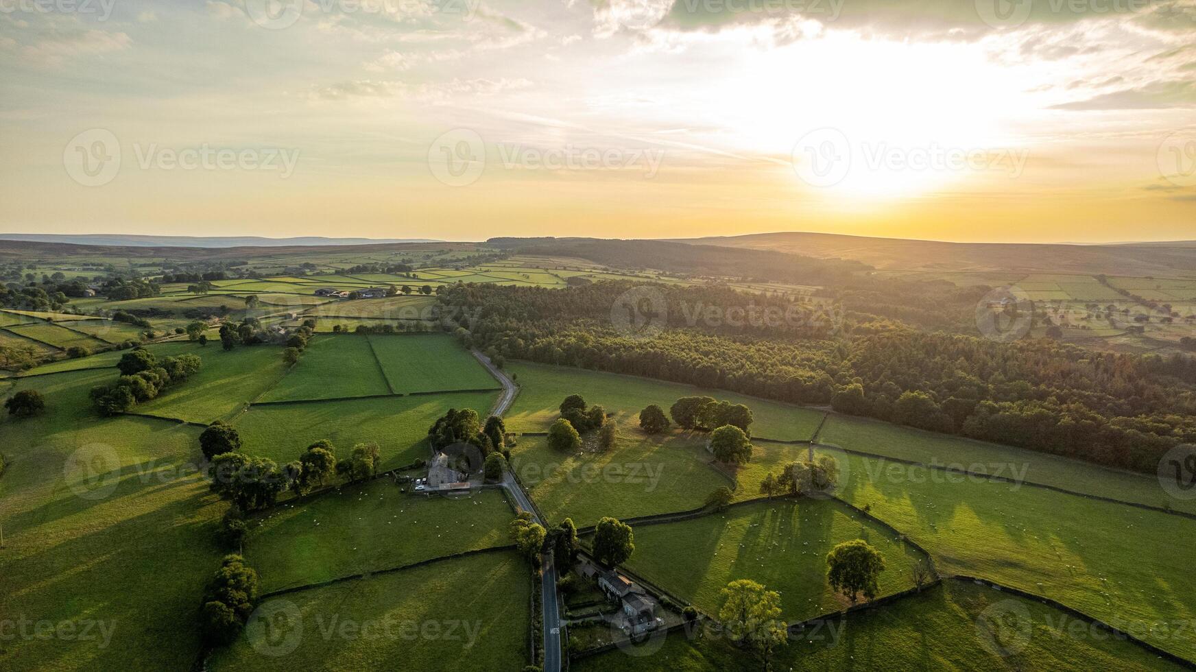 Aerial view of a lush countryside at sunset with vibrant green fields and a golden sky. photo