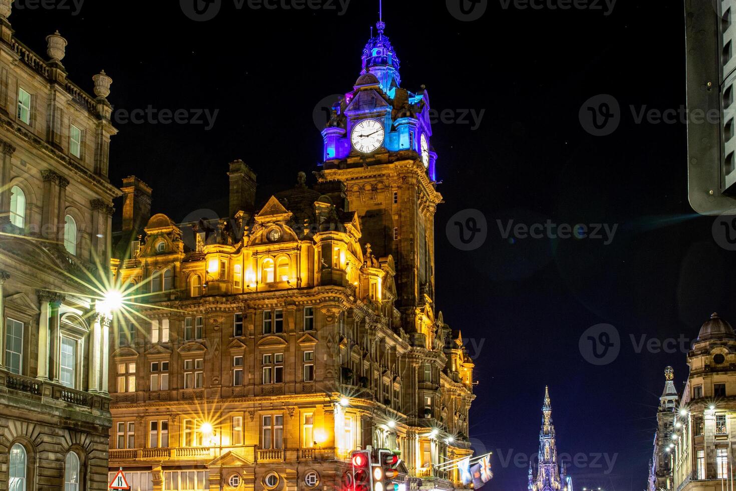 Illuminated historic building at night with clock tower, city lights, and clear sky. photo