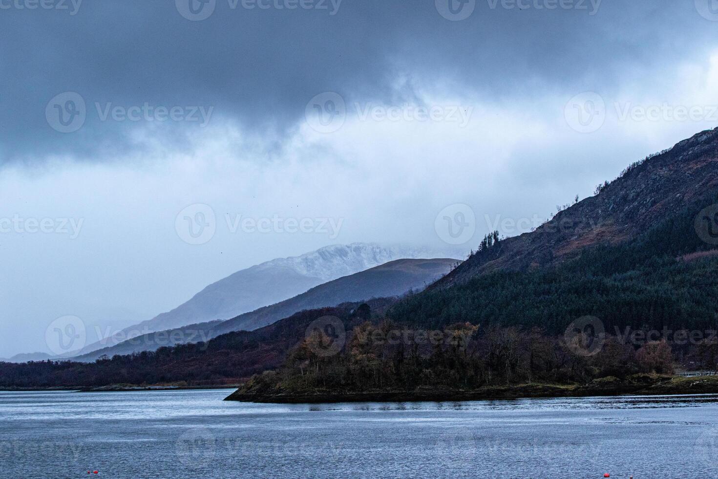 Misty mountain landscape with lake in the foreground under overcast sky in Scotland. photo