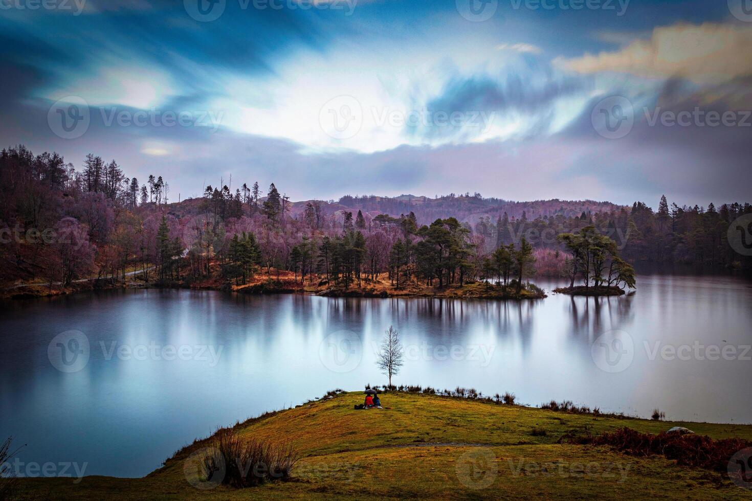 Serene lake with reflection of autumn trees under a dynamic blue sky with clouds at dusk. photo