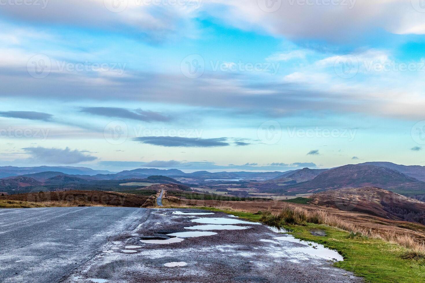 Scenic view of a winding road through rolling hills under a vast blue sky with clouds. photo